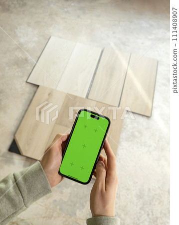 Hands Holding Device with Green Chroma Key Screen above Luxury Vinyl Wood Samples, Laminate On Floor In House. Choosing, Selecting Waterproof Flooring. Home Reconstruction. Vertical Plane Hands Holding Device with Green Chroma Key Screen above Luxury Vinyl Wood Samples, Laminate On Floor In House. Choosing, Selecting Waterproof Flooring. Home Reconstruction. Vertical Plane 111408907