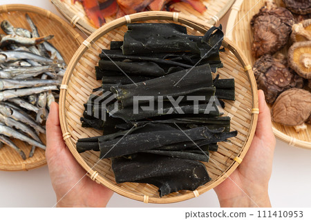 A woman's hands hold konbu root, dried sardines, dried shiitake mushrooms, and thickly shaved bonito flakes 111410953