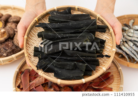 A woman's hands hold konbu root, dried sardines, dried shiitake mushrooms, and thickly shaved bonito flakes 111410955