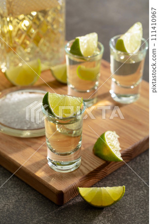Tequila with sea salt and lime slices on a cutting board. Tequila with sea salt and lime slices on a cutting board. 111410967