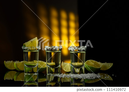 Tequila with sea salt and lime slices on a black reflective background. Tequila with sea salt and lime slices on a black reflective background. 111410972