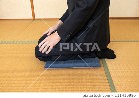 一個穿著黑色西裝的男人坐在墊子上 一個穿著黑色西裝的男人坐在墊子上 111410980