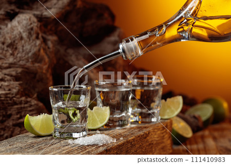 Tequila is poured from a bottle into a glass. Tequila is poured from a bottle into a glass. 111410983