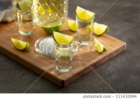 Tequila with sea salt and lime slices on a cutting board. Tequila with sea salt and lime slices on a cutting board. 111410994