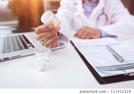 The doctor writes a prescription holding pills in his hand 111412329