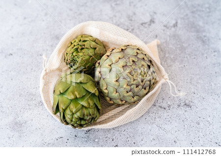 Top view of artichoke in linen eco bag on table. Flat lay of Healthy food vegetables. Top view of artichoke in linen eco bag on table. Flat lay of Healthy food vegetables. 111412768