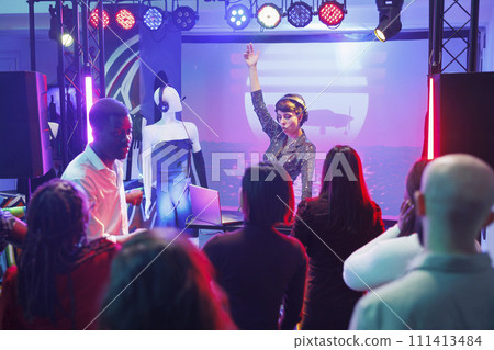 Woman using dj station and software on laptop to mix tracks on stage at disco party in nightclub. Musician playing electronic music at discotheque while people dancing in club 111413484