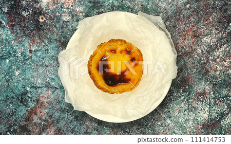 One Pastel de nata or Portuguese egg tart on a white plate. Pastel de Belm is a small pie with a crispy puff pastry crust and a custard cream filling One Pastel de nata or Portuguese egg tart on a white plate. Pastel de Belm is a small pie with a crispy puff pastry crust and a custard cream filling 111414753