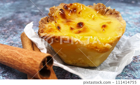 One Pastel de nata or Portuguese egg tart and cinnamon sticks. Pastel de Belm is a small pie with a crispy puff pastry crust and a custard cream filling 111414755