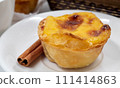 Plate with one Portuguese Pastel de Nata pie with custard and cinnamon sticks. Pastel de Belem is an iconic cup-shaped pastry with a burnt top and a crispy puff pastry crust. Sweet dessert 111414863