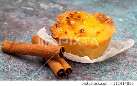 One Pastel de nata or Portuguese egg tart and cinnamon sticks. Pastel de Belm is a small pie with a crispy puff pastry crust and a custard cream filling 111414886
