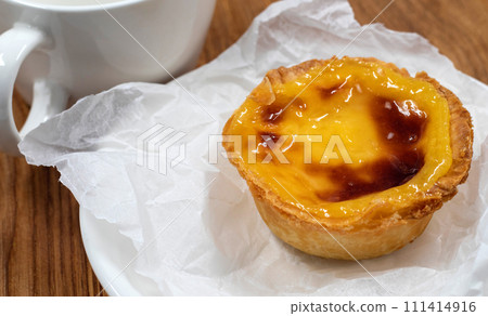 One Pastel de nata or Portuguese egg tart on a white plate. Pastel de Belm is a small pie with a crispy puff pastry crust and a custard cream filling 111414916