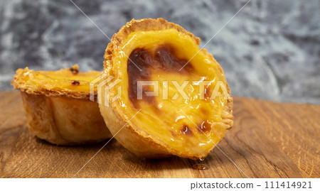 Pastel de nata tarts or Portuguese egg tart on a wooden brown background. Pastel de Belem is a small pie with a crispy puff pastry crust and a custard cream filling. Sweet dessert 111414921