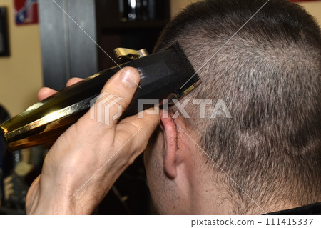 A hairdresser cuts hair on a client's head with a clipper. 111415337