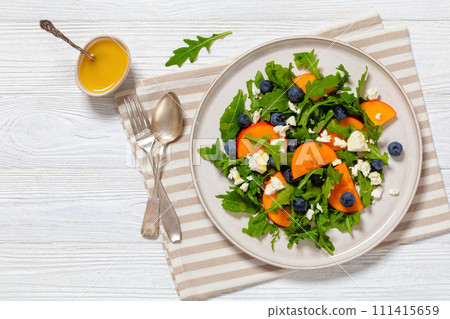 arugula persimmon cheese berries salad, top view arugula persimmon cheese berries salad, top view 111415659