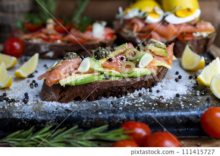 Salted salmon open sandwich with guacamole, avocado, olives, cheese, pesto and garlick. Healthy seafood Salted salmon open sandwich with guacamole, avocado, olives, cheese, pesto and garlick. Healthy seafood 111415727
