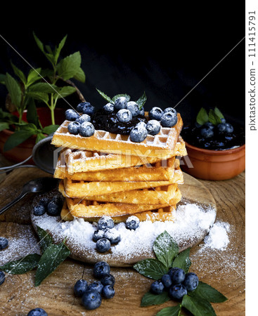 Waffles with fresh blueberries and powdered sugar on the rustic table. Freshly made Belgian waffles Waffles with fresh blueberries and powdered sugar on the rustic table. Freshly made Belgian waffles 111415791