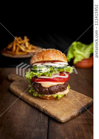 Burger with beef meat, cheese, lettuce, onion, tomato, cucumber, mayo and ketchup on an old wooden table. Junk food concept 111415952