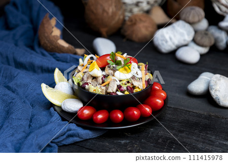 Fish salad with sardines, harringe, tuna, tomato, lemon, lettuce, cabbage, olives, beans, corn, carrotes and eggs on rustic kitchen table 111415978