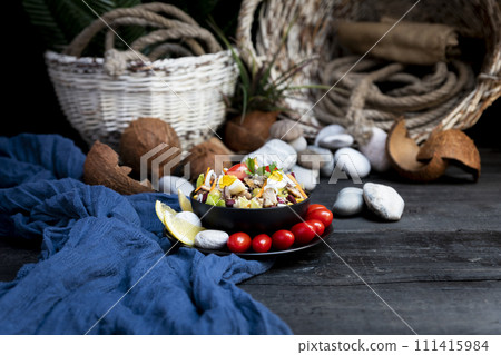 Fish salad with sardines, harringe, tuna, tomato, lemon, lettuce, cabbage, olives, beans, corn, carrotes and eggs on rustic kitchen table 111415984