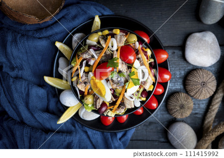 Fish salad with sardines, harringe, tuna, tomato, lemon, lettuce, cabbage, olives, beans, corn, carrotes and eggs on rustic kitchen table. Fresh and delicous seafood. Top view photo 111415992