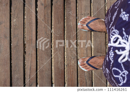 Mans feet in flip flops on wooden boardwalk. Top view. Flat lay. Empty space, for text 111416261