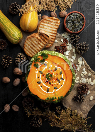 Pumpkin soup with pumpkin seeds, cream, parsley and spices on the rustic kitchen table. Flat lay. Top view 111416329