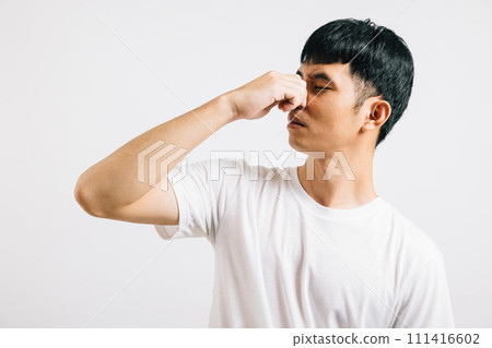 A disgusted Asian man holds his nose, expressing strong displeasure due to a bad smell situation. Studio shot isolated on white background, showcasing his humorous reaction. 111416602