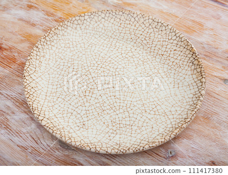 Empty hand-crafted ceramic plate on wooden table surface 111417380
