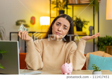 Poor Caucasian young woman holding piggybank and one dollar insufficient amount of money poverty Poor Caucasian young woman holding piggybank and one dollar insufficient amount of money poverty 111417451