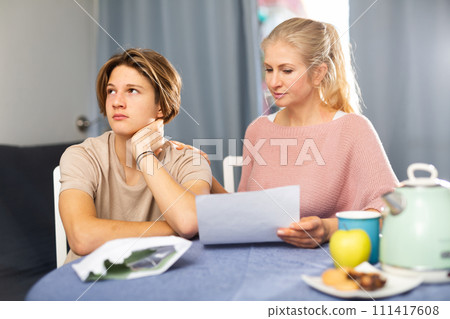 Unhappy mother and son reading letter from school 111417608