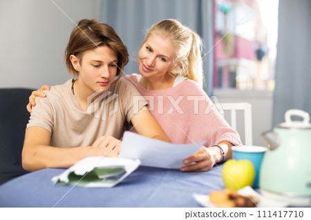 Happy woman with teenage son reading letter with good news Happy woman with teenage son reading letter with good news 111417710
