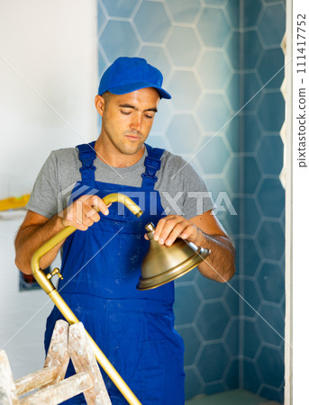 Young man builder in work clothes working in bathroom holding shower head Young man builder in work clothes working in bathroom holding shower head 111417752