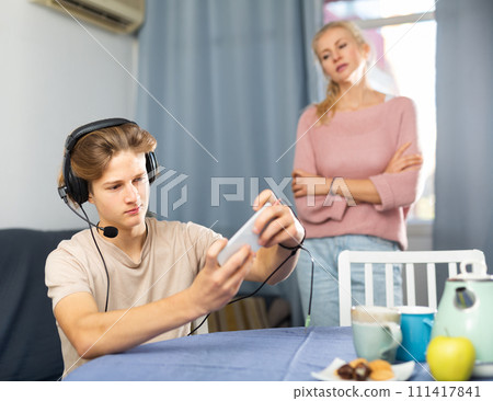 Teen boy with smartphone not paying attention to upset mother Teen boy with smartphone not paying attention to upset mother 111417841