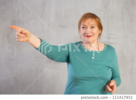 Amiable elderly woman in teal jumper pointing towards 111417952
