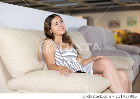 Young woman testing softness of sofa in furniture salon 111417990