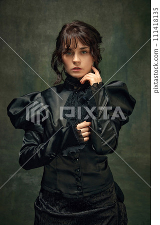 Portrait of beautiful, elegant young woman in Victorian black dress standing against dark vintage green textured background. 111418135