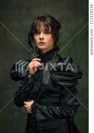 Portrait of beautiful, elegant young woman in Victorian black dress standing against dark vintage green textured background. 111418138