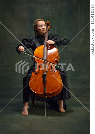 Beautiful woman, talented, passionate cellist looking upward and playing cello against vintage green background. Breathtaking moment 111418156