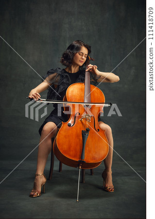 Cellist, elegant woman in deep concentration, playing cello passionately with eyes closed against vintage green background. Cellist, elegant woman in deep concentration, playing cello passionately with eyes closed against vintage green background. 111418709