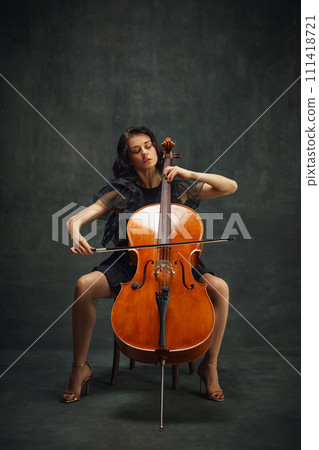 Elegant, passionate musician, beautiful woman in black dress sitting and playing cello against dark green vintage background. Elegant, passionate musician, beautiful woman in black dress sitting and playing cello against dark green vintage background. 111418721