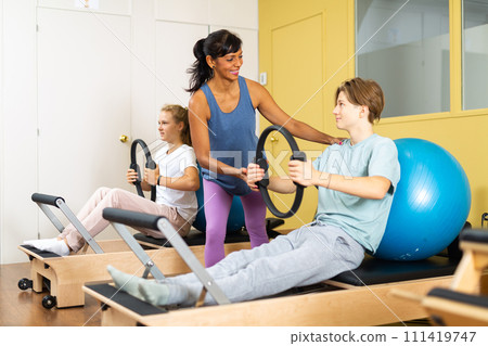 Pilates instructor helps teenager do exercises with ring Pilates instructor helps teenager do exercises with ring 111419747