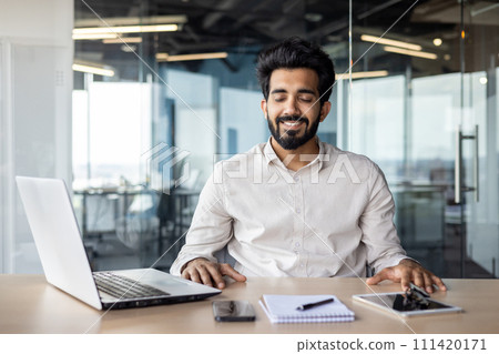Indian businessman in a modern office working on a laptop with a cheerful disposition, portraying professionalism and focus. 111420171