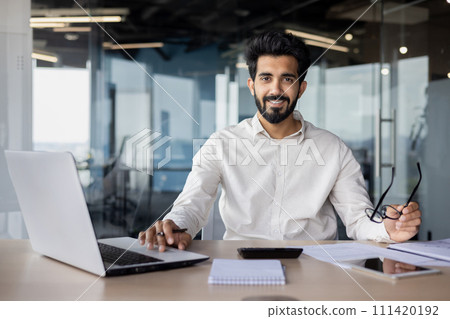 A white-collar worker is sitting at a desk with a laptop and wearing glasses, working on an engineering project with office equipment. A white-collar worker is sitting at a desk with a laptop and wearing glasses, working on an engineering project with office equipment. 111420192