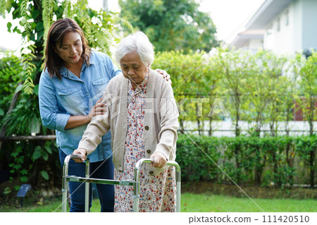 Caregiver help Asian elderly woman disability patient walk with walker in park, medical concept. Caregiver help Asian elderly woman disability patient walk with walker in park, medical concept. 111420510