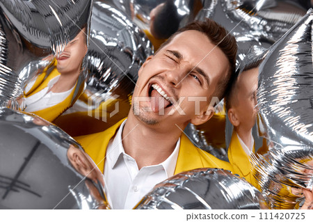 happy winking man in yellow jacket with a lot of silver air balloons. birthday party 111420725
