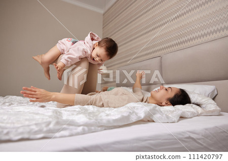 Happy Caucasian mother raising laughing cute baby daughter and playing together in bedroom Happy Caucasian mother raising laughing cute baby daughter and playing together in bedroom 111420797