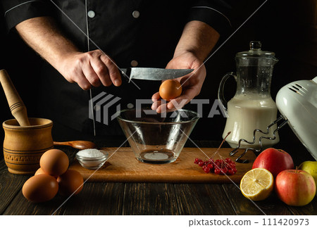 The cook prepares an egg omelette with milk in the kitchen of a breakfast restaurant. Work environment on kitchen table with fruits and eggs. Knife in the hand of a chef 111420973