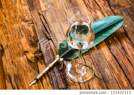 Small shot glass on the old bar counter. Vintage wooden background in pub or bar, night mood. Place for text, toning Small shot glass on the old bar counter. Vintage wooden background in pub or bar, night mood. Place for text, toning 111422113