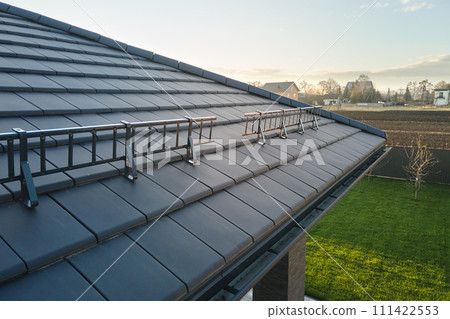 Closeup snow guard for safety in winter on house roof top covered with ceramic shingles. Tiled covering of building 111422553
